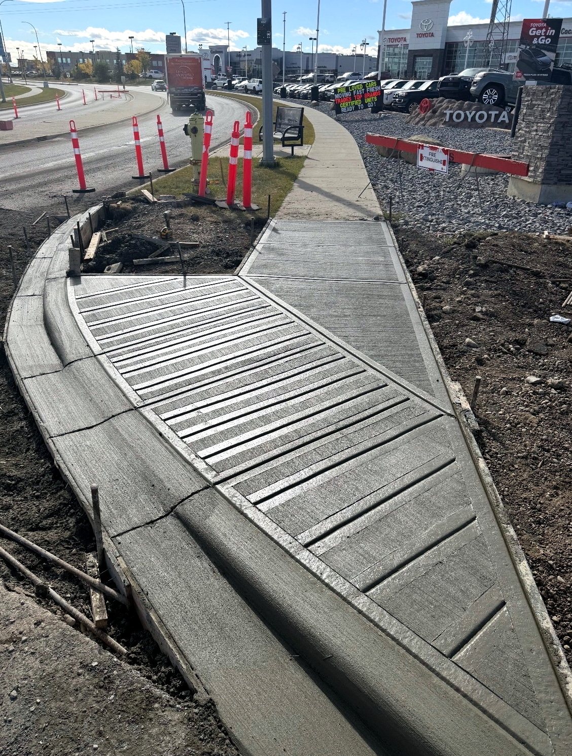 Grooved concrete curb ramp with traction strips connecting a broom-finished commercial sidewalk at the Cochrane Toyota dealership, installed by SiteWorx Concrete