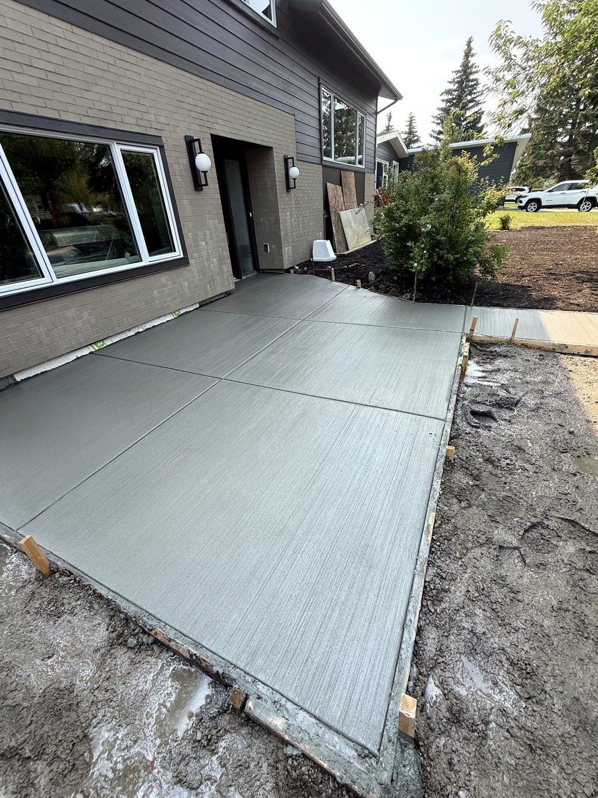 Large broom-finished concrete patio with saw-cut control joints at the entrance of a modern grey Calgary home, poured by SiteWorx Concrete