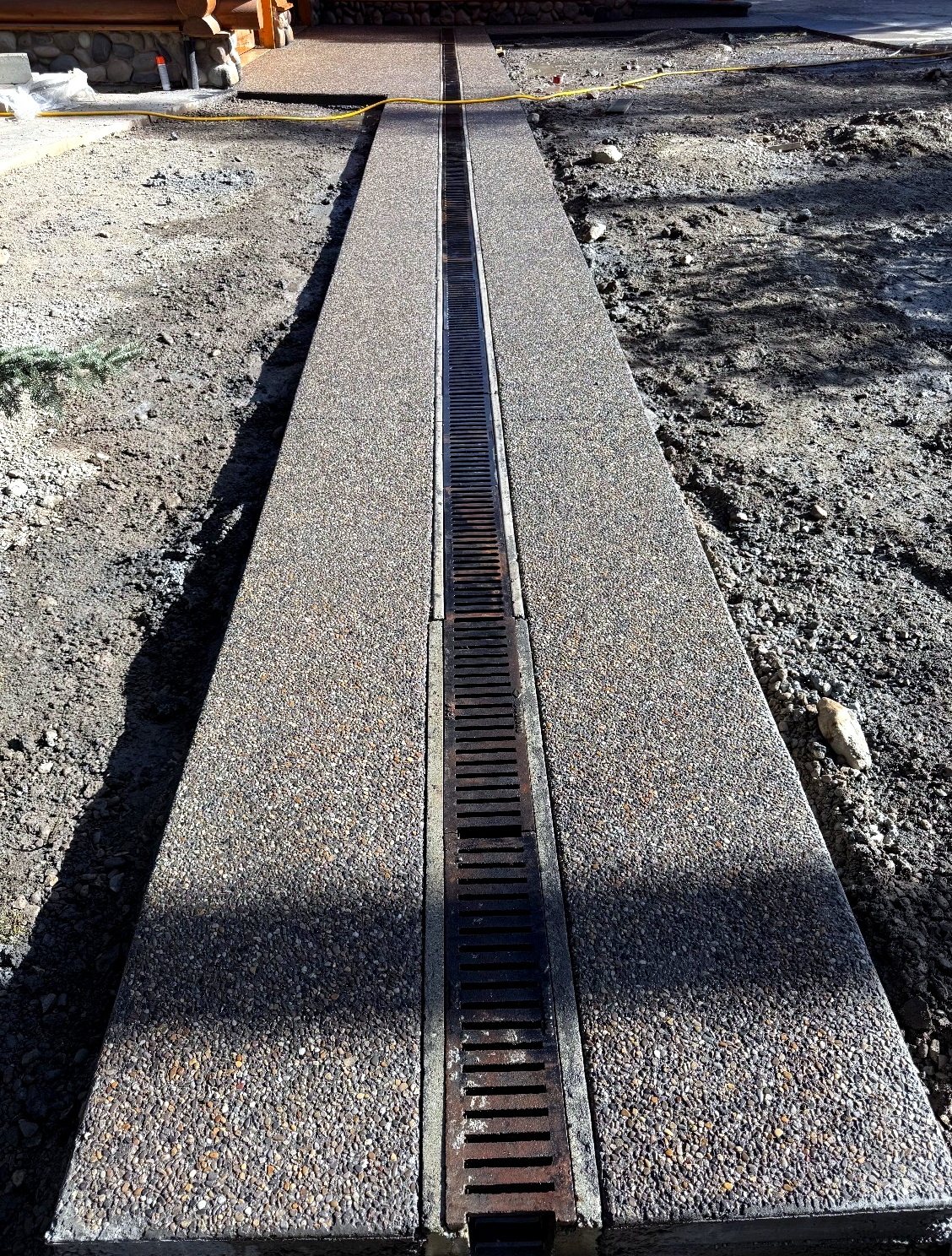Close-up of a full-length channel drain grate set into an exposed aggregate concrete driveway at a Calgary area log home, installed by SiteWorx Concrete