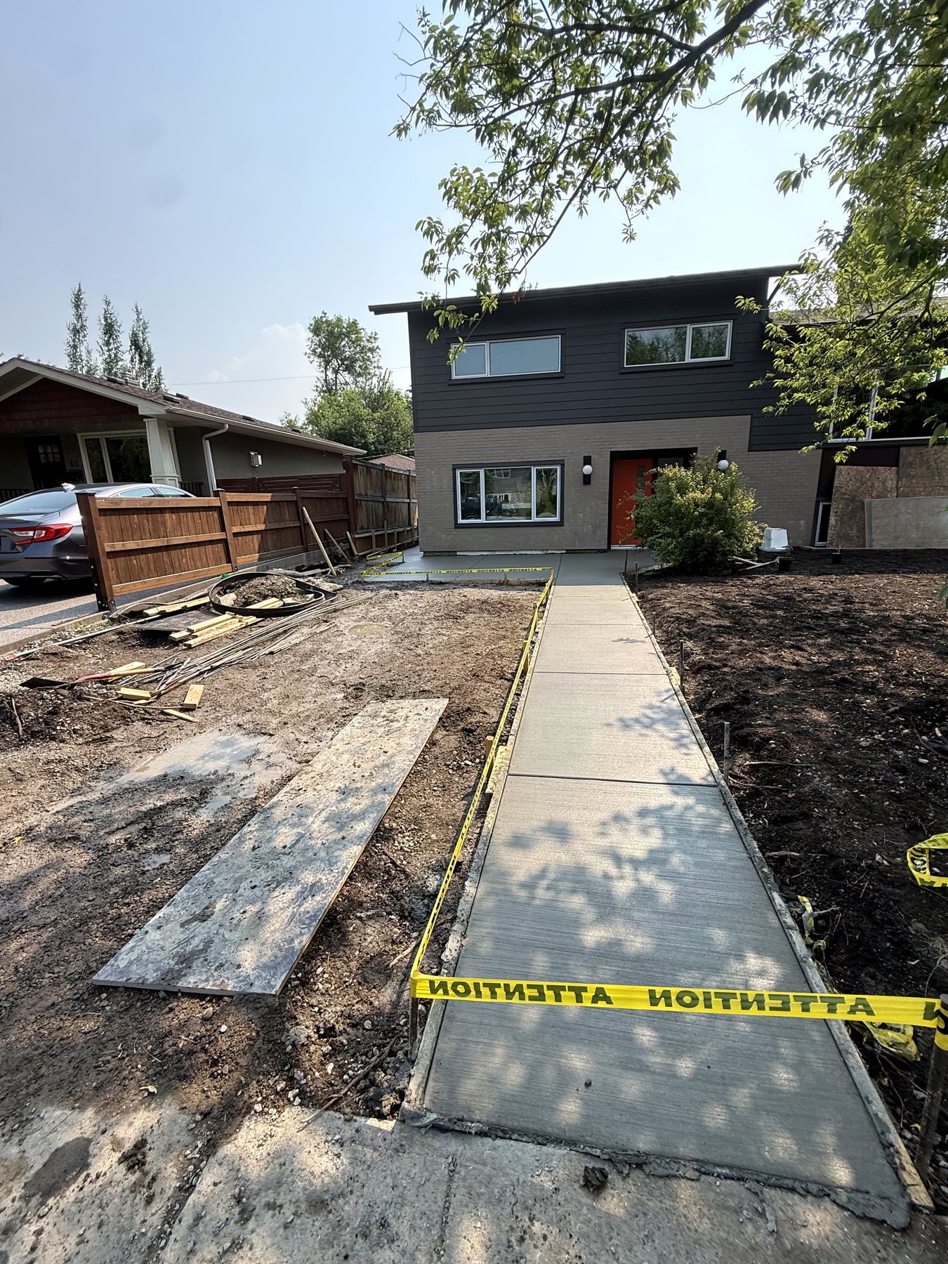Freshly poured broom-finished residential concrete walkway with forms and caution tape alongside a modern Calgary home, installed by SiteWorx Concrete