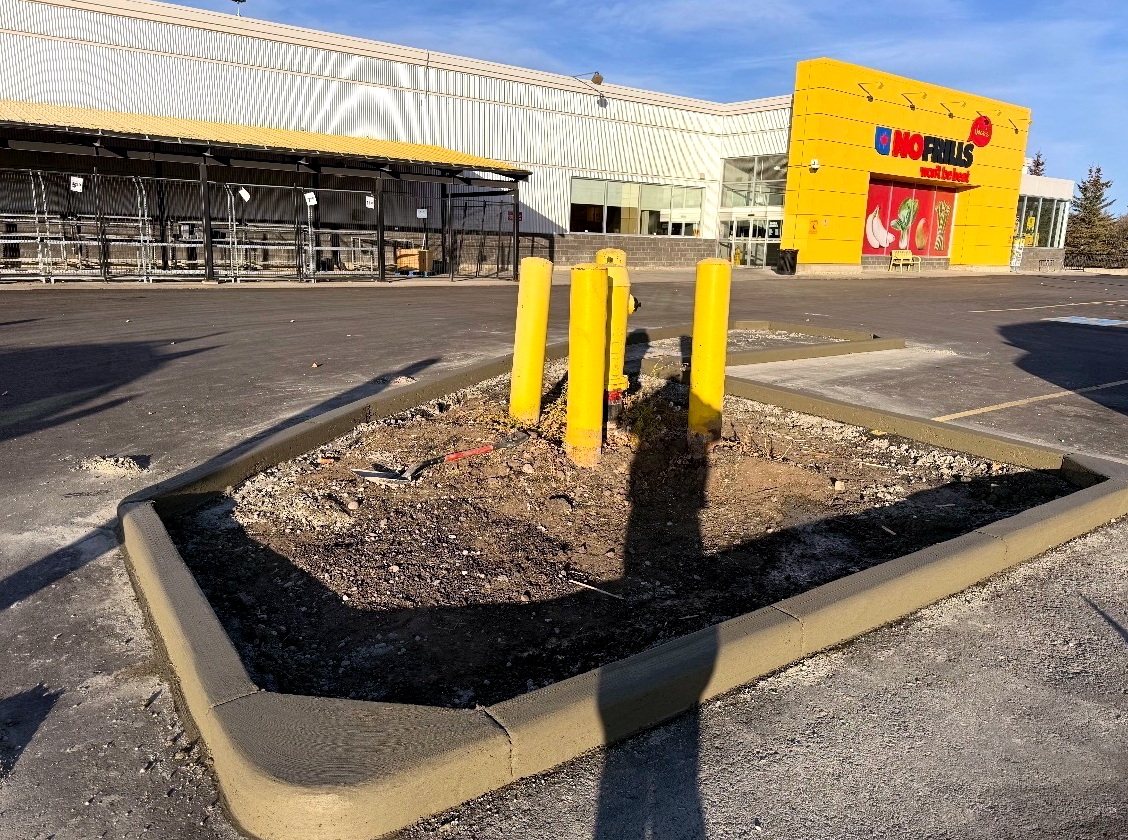 Concrete parking lot curb island with yellow safety bollards around a fire hydrant at a No Frills grocery store, installed by SiteWorx Concrete