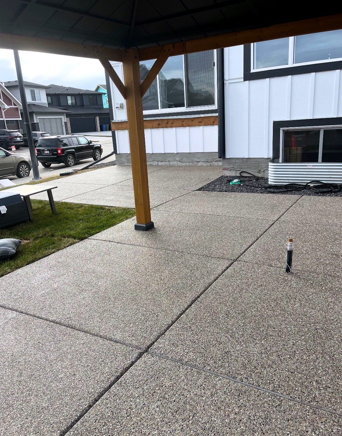 Covered exposed aggregate concrete patio slab with saw-cut control joints under a timber post awning at a Calgary home, installed by SiteWorx Concrete