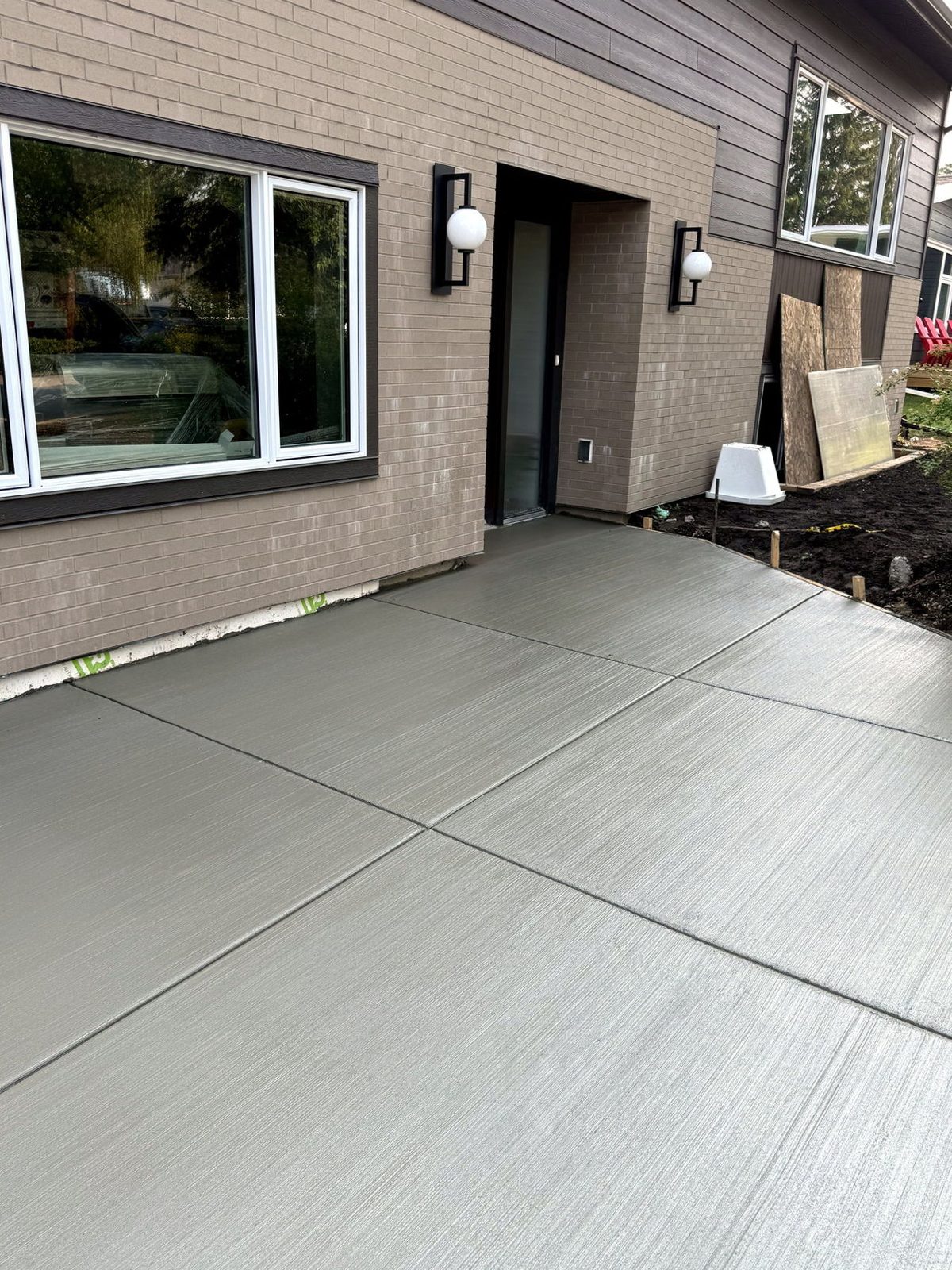 Finished broom-finished concrete patio and walkway with saw-cut joints at the front entrance of a modern brick Calgary home, installed by SiteWorx Concrete