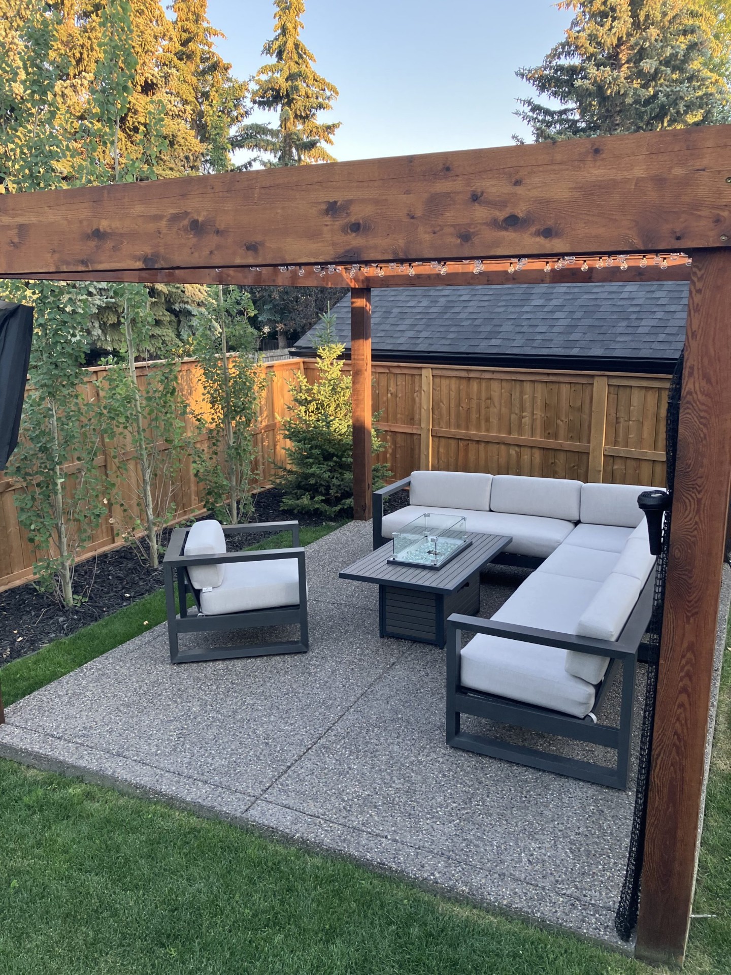Exposed aggregate concrete patio with wooden pergola, string lights and outdoor lounge furniture by SiteWorx Concrete Calgary