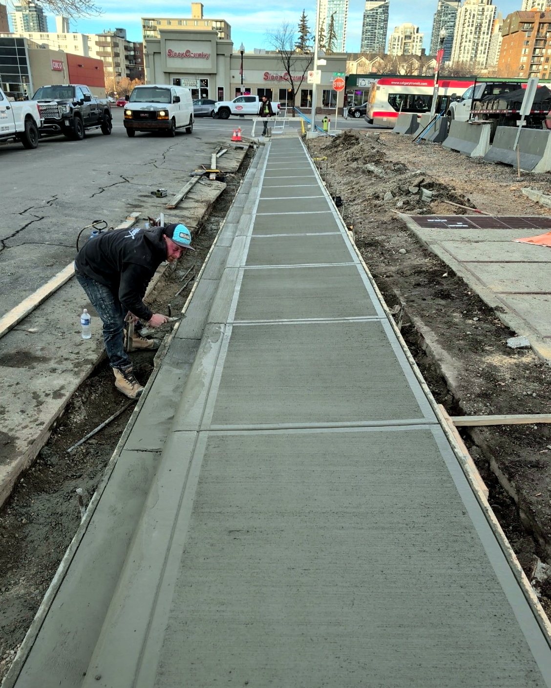 SiteWorx Concrete finisher hand-edging a freshly poured broom-finished commercial sidewalk along a Calgary retail street