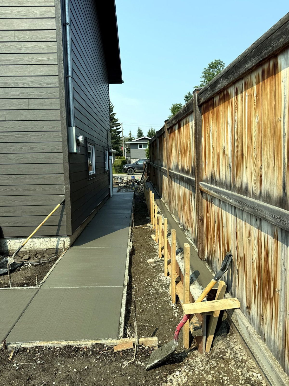 Freshly poured broom-finished concrete side-yard patio walkway along a wood fence with forms in place at a Calgary home, installed by SiteWorx Concrete