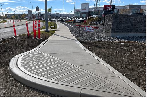 Freshly poured broom-finished commercial concrete sidewalk with contrast border along Toyota dealership frontage by SiteWorx Concrete