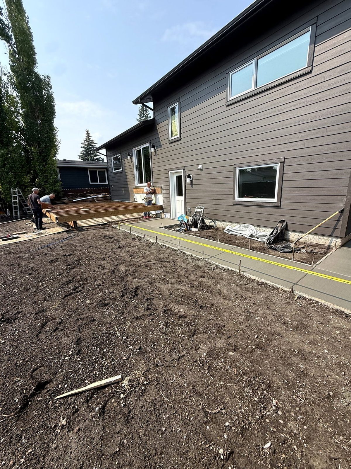 Freshly poured broom-finished concrete backyard patio border and walkway alongside a modern Calgary home during deck construction, installed by SiteWorx Concrete